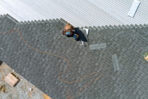 A asphalt shingles installation on the roof roofer is nailing asphalt shingles to roofing construction